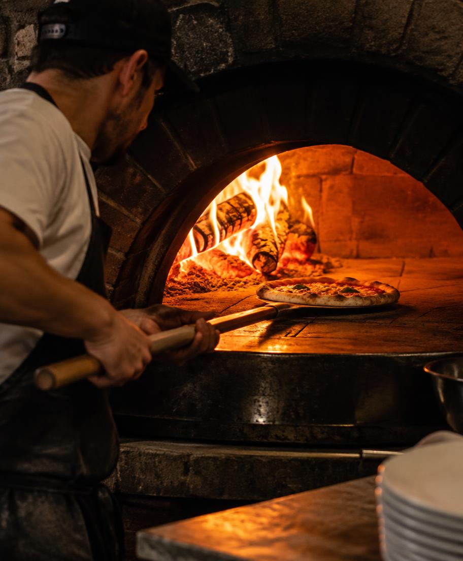 Pizzabäcker schiebt eine Pizza in den Holzofen